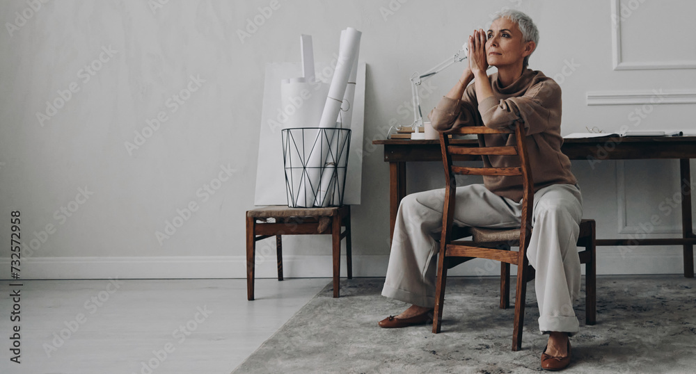 Beautiful senior woman looking thoughtful while sitting at her creative working place