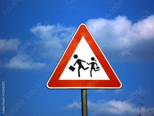 Road sign warning schools nearby, students crossing the road with blue sky in the background