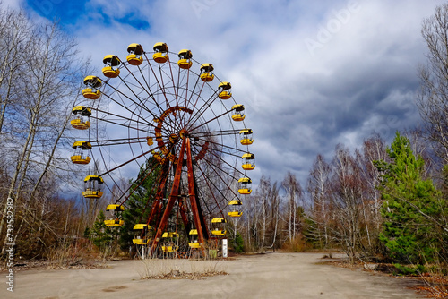 Yellow cabins of an abandoned Ferris wheel amidst overgrown vegetation.