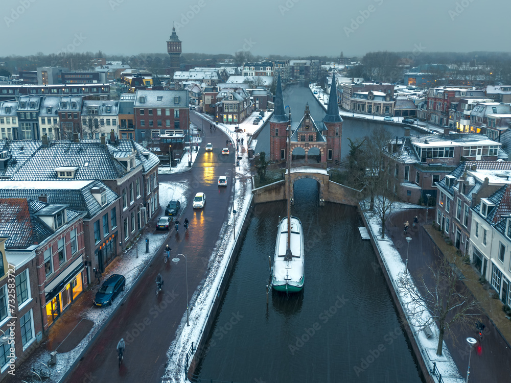 Aerial drone image of the historic Water gate, waterpoort, in Sneek, Friesland, the Netherlands, in winter with light layer of fresh white snow. With traditional wooden flat bottomed boat, a skutsje.
