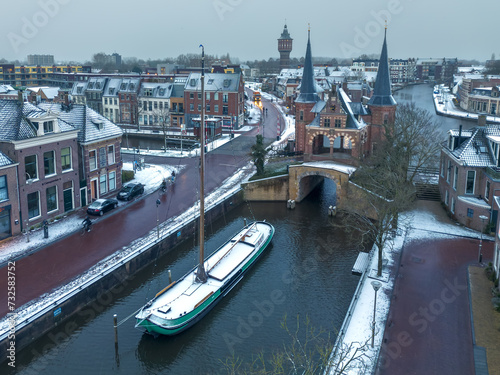 Aerial drone image of the historic Water gate, waterpoort, in Sneek, Friesland, the Netherlands, in winter with light layer of fresh white snow. With traditional wooden flat bottomed boat, a skutsje.