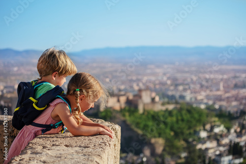 Blond siblings stand on viewpoint admire Alhambra castle