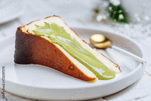 Popular Spanish dessert called San Sebastian cheesecake. It also known as burnt cheesecake. One piece of this dessert on white background with pistachio glaze on it.