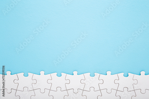 Row of completed different white puzzle pieces on light blue table background. Pastel color. Closeup. Empty place for text. Top down view.