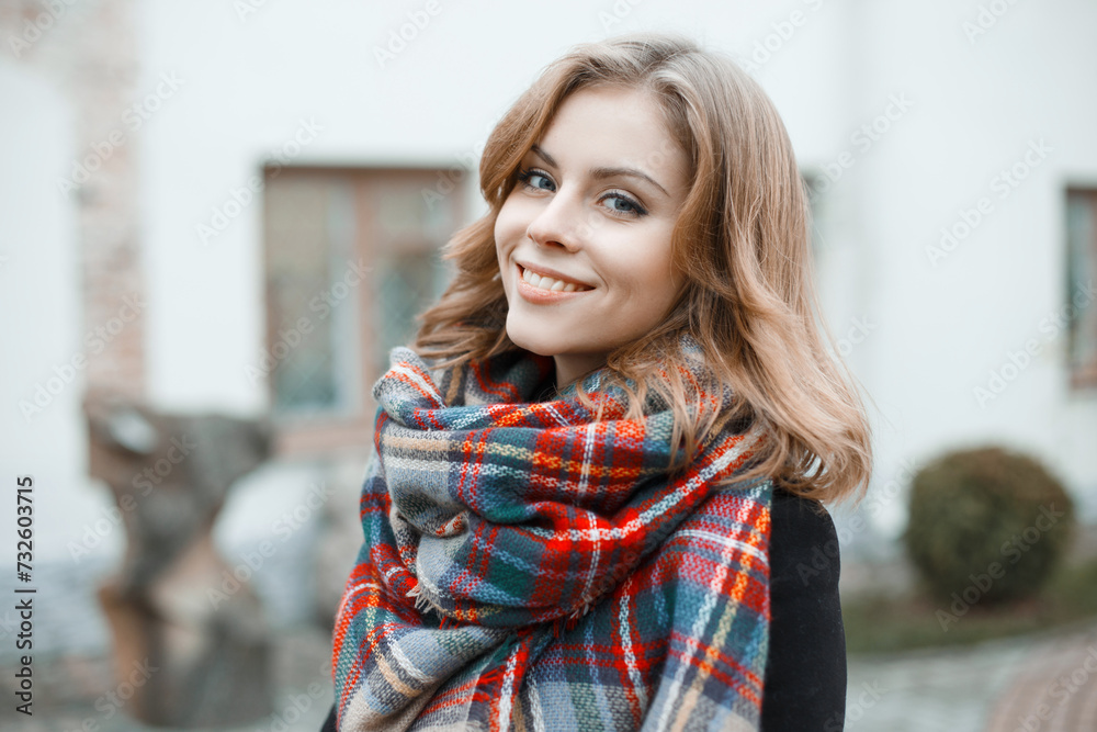 Beautiful young woman with a sweet smile with a vintage plaid fashion coat walks in the city and looks at the camera Beautiful young woman with a sweet smile with a vintage plaid fashion coat walks in the city and looks at the camera