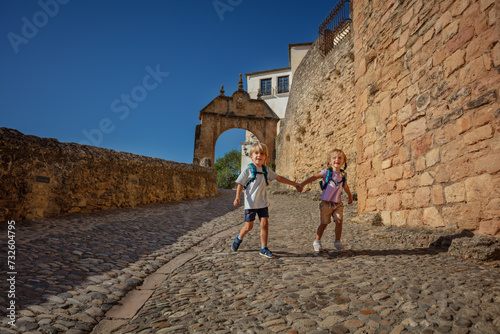 Happy children with backpack run paved street of Ronda, Spain