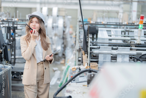 Asian female engineer manager holding radio and tablet Wear a safety helmet and suit in the plastic and steel manufacturing industry used to make export robots and machines are working.