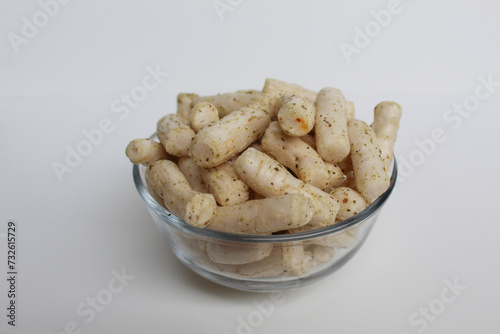 Fish crackers in small cylinder shape. Snack from Indonesia, called krupuk ikan tongkol. In a transparent glass bowl, isolated on white background