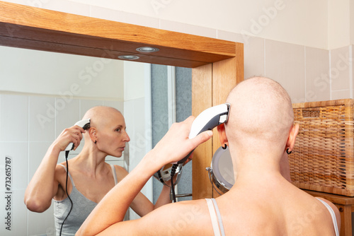 Strong woman focused on shaving head using mirror for guidance
