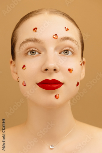 Beautiful girl with glitter on her face on peach isolated background. Happy woman in love with red lipstick. Valentine's day concept. International women's day. Vertical photo. Advertisement