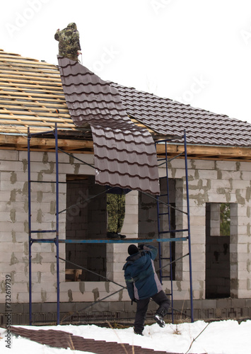 Workers install tiles on the roof of a house in winter