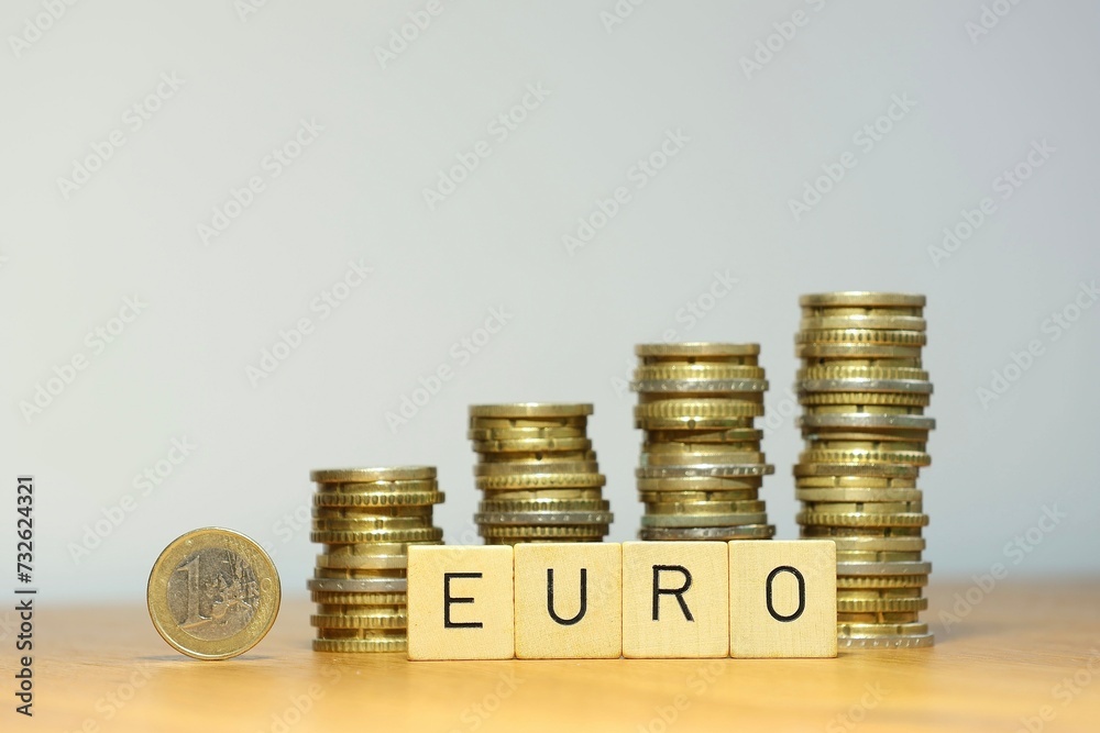 Steigender Eurokurs symbolisiert durch eine Euro Geldmünze, Stapel aus Münzgeld und den Schriftzug Euro, die Währung Euro gewinnt an Wert durch finanziellen Aufschwung, steigendes Gehalt und mehr Geld - obrazy, fototapety, plakaty 