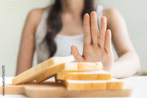 Gluten allergy, asian young woman hand push out, refusing to eat white bread slice on chopping board in food meal at home, girl having a stomach ache. Gluten intolerant and Gluten free diet concept. photo