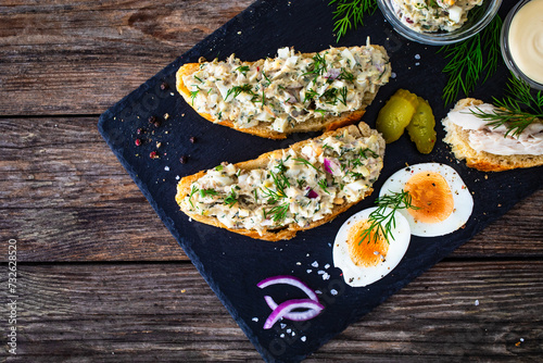 Tasty sandwich with egg salad and smoked mackerel on wooden table 