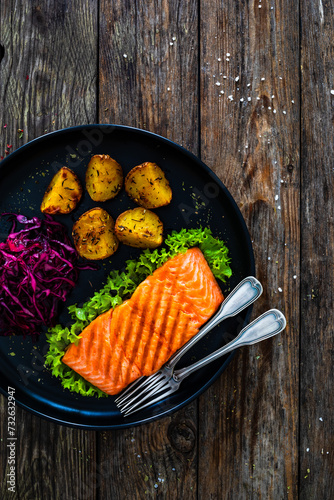 Grilled salmon steak with baked potatoes and  red cabbage  on black plate on wooden table
