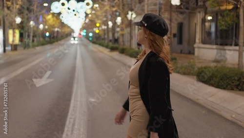 American side shot in motion of a pretty woman in a black coat and light brown dress crossing a street