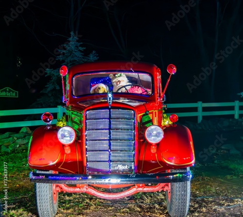 Vintage Red Mack Truck Decorated With Christmas Lights And Wreaths, Featuring Stuffed Animal Passengers In The Front Seat, Parked At Night. photo