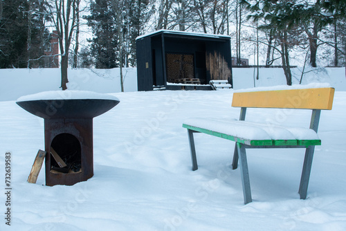 Metal campfire and colorful wooden bench covered in snow in a park in Finland during an overcast day in winter