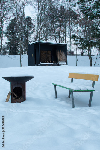 Metal campfire and colorful wooden bench covered in snow in a park in Finland during an overcast day in winter