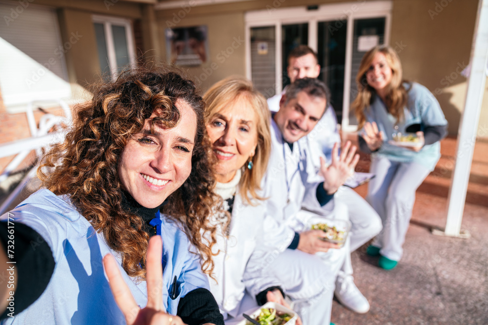 Obraz premium Outdoor gathering of medical staff, with one nurse standing and talking, while others sit, enjoying healthy snacks and engaging discussions