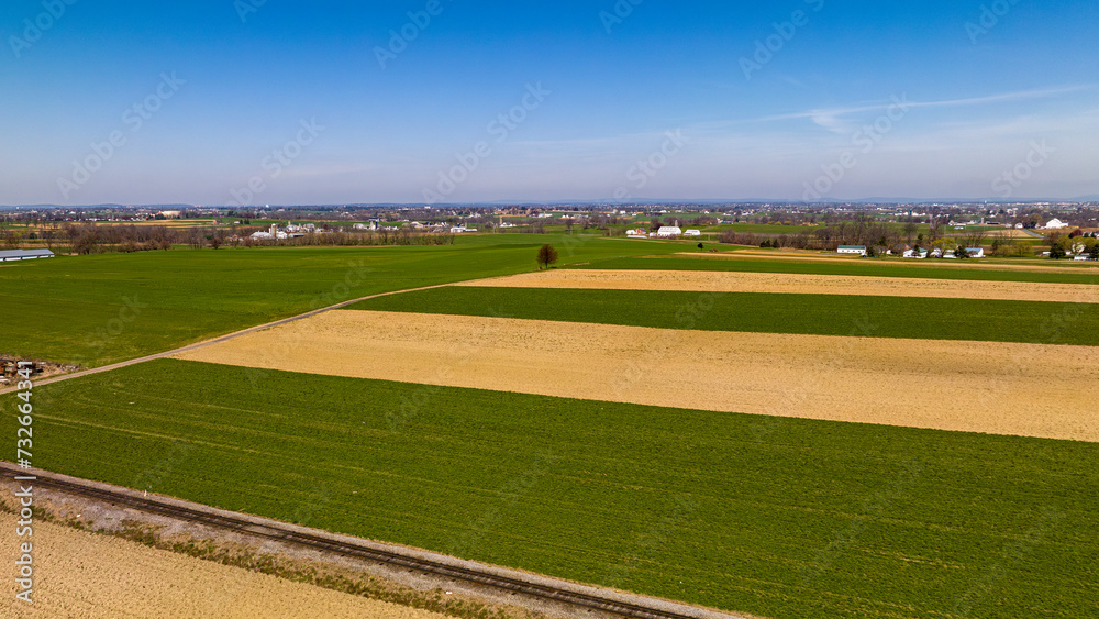 Vast Agricultural Fields With Distinctive Green And Beige Patterns Bordering A Small Town Under The Expansive Blue Sky. Vast Agricultural Fields With Distinctive Green And Beige Patterns Bordering A Small Town Under The Expansive Blue Sky.