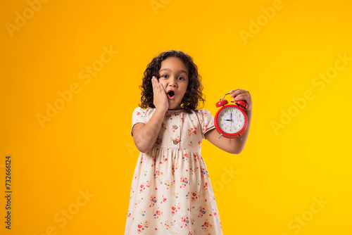Surprised kid girl holding an alarm clock in hand. The concept of education, school, deadlines, time to study