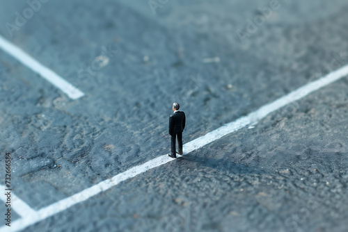 toy businessman standing in a white line crossing an  photo