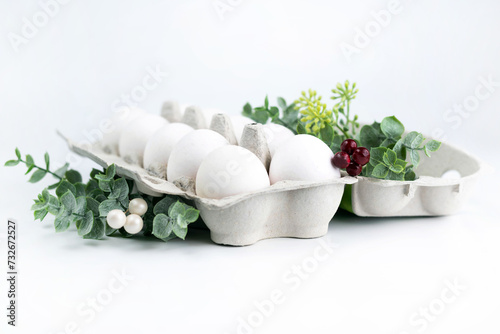 White eggs in a tray and sprigs of greenery on a white background. Easter concept.
