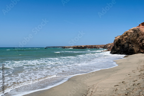 The Atlantic Ocean in Jandia with clear sky and mountains in the back and waves breaking on the shore