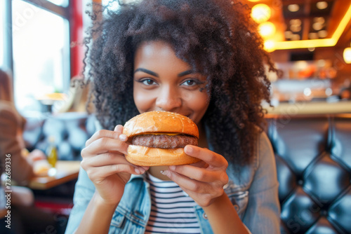 young African American woman, sitting in a restaurant, eating a tasty and perfect burger,