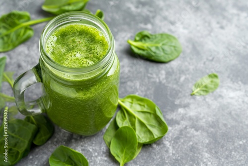 Green detox smoothie in a jar surrounded by basil leaves on a grey background with space for text