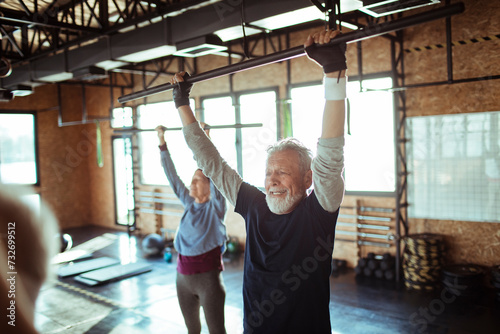 Senior man and woman exercising in gym doing pull-ups photo