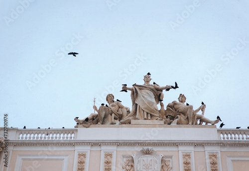 Roof of Ivan Franko University in Lviv, Ukraine. A flock of crows flies against the sky near sculptures dedicated to Galicia and the Dniester and Vistula rivers. photo