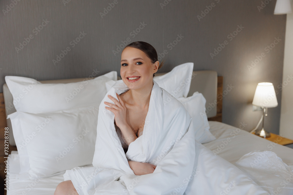 Smiling Woman Wrapped in White Duvet Sitting on Bed in Modern Room of hotel, concept wedding morning Smiling Woman Wrapped in White Duvet Sitting on Bed in Modern Room of hotel, concept wedding morning