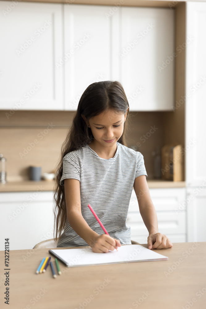 Positive pretty little kid girl drawing in colored pencils at kitchen table, enjoying creativity, artistic hobby, doing art school homework task, scratching doodles in paper album Positive pretty little kid girl drawing in colored pencils at kitchen table, enjoying creativity, artistic hobby, doing art school homework task, scratching doodles in paper album