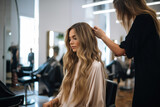An attractive woman with long, wavy hair at a professional hairdressing salon, receiving stylish treatment.