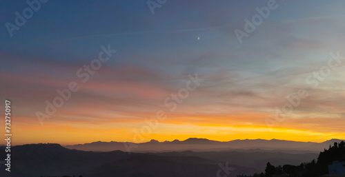 Tramonto cobalto e arancio con luna nel cielo sopra le valli e le montagne