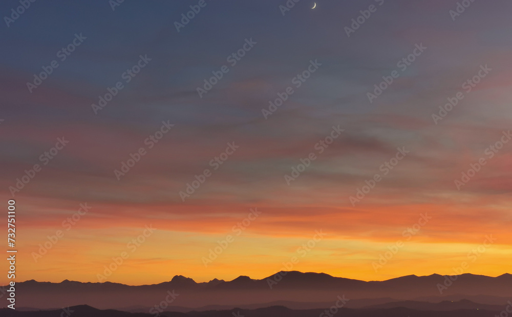 La Luna al tramonto nel cielo arancione sopra le montagne - obrazy, fototapety, plakaty 