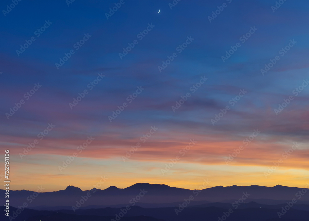 Tramonto blu e arancio con luna nel cielo sopra le valli e le montagne