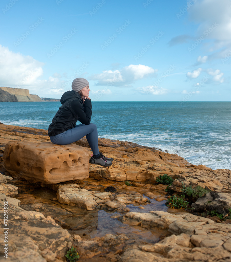 woman walker sitting on a rock enjoying the view of the sea.
