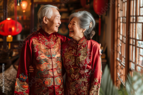 An elderly Asian couple in traditional red attire share a joyful moment, surrounded by cultural decor and red lanterns. © AIPhoto
