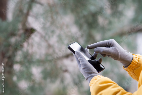 close up of woman in jacket using smartphone with touchscreen gloves, female hands with touchscreen gloves holding smartphone