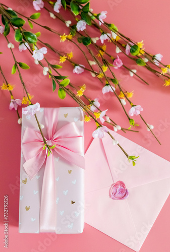 One gift box with an envelope and branches of spring flowers on a pink background.