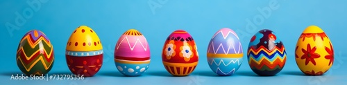 A collection of Easter eggs, each painted in bright, primary colors with bold, graphic designs, set against a sky blue background. photo