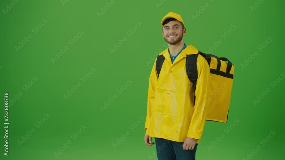 Green Screen Young Food Delivery Person in Yellow Uniform and With a Thermal Backpack and Using Smartphone to Check Order. Courier On the Way to Deliver Order to Client. Back View Green Screen Young Food Delivery Person in Yellow Uniform and With a Thermal Backpack and Using Smartphone to Check Order. Courier On the Way to Deliver Order to Client. Back View