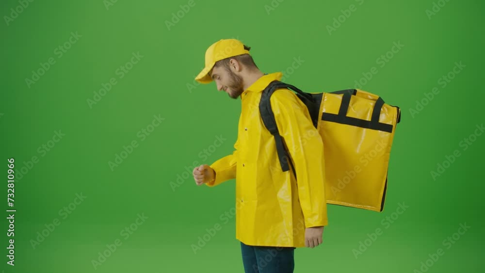 Green Screen Young Food Delivery Person in Yellow Uniform and With a Thermal Backpack and Using Smartphone to Check Order. Courier On the Way to Deliver Order to Client. Back View