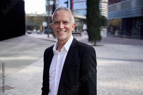 Portrait of attractive mature business man grizzled executive smiling looking at camera standing outside office building. Senior CEO professional formal manager confident posing in suit. Copy space 