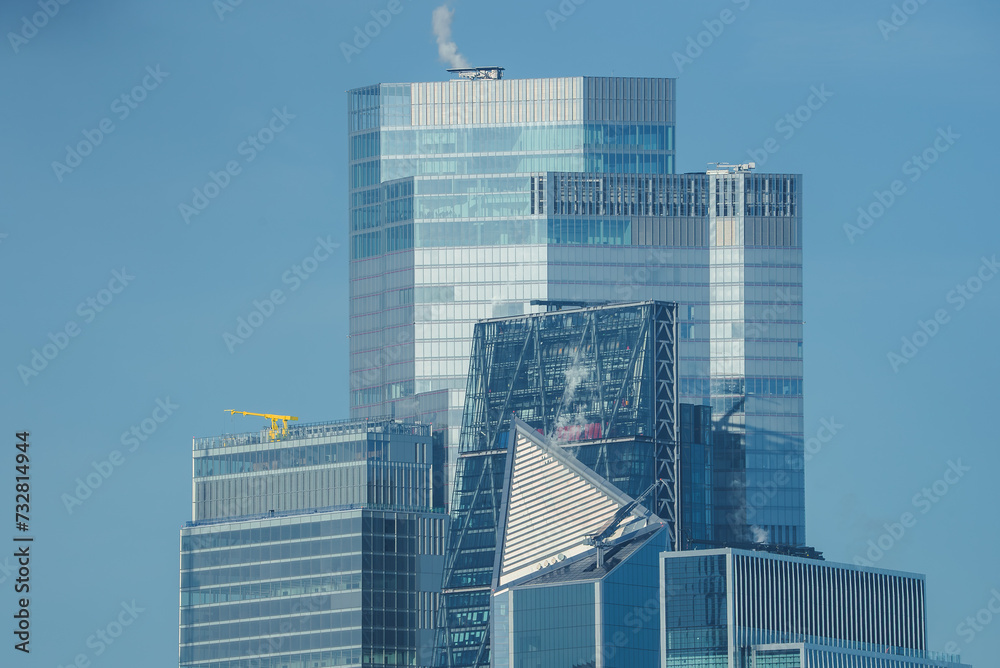 A clear blue sky backdrop highlights the modern glass skyscrapers of London's business district, featuring geometric designs and a distinctive sloped building.
