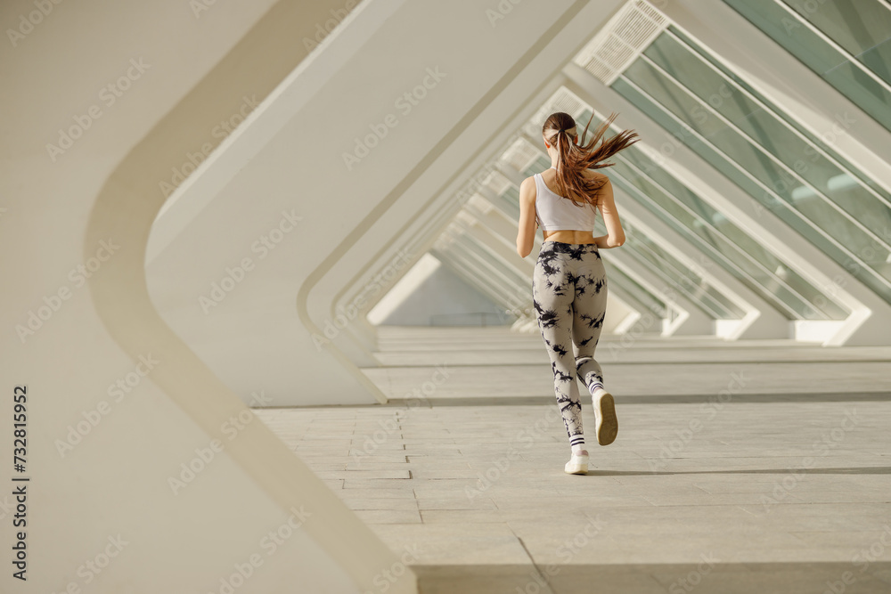 Young woman in sportswear is running on modern buildings background. Active lifestyle concept Young woman in sportswear is running on modern buildings background. Active lifestyle concept