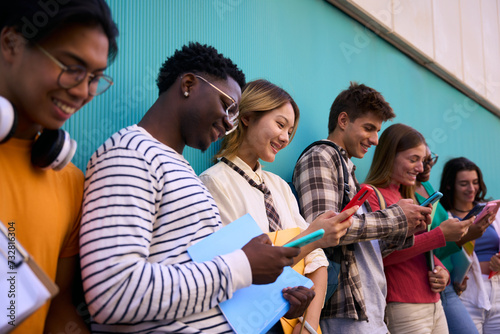 Group of young international university students smile happily watching funny videos on a smartphone holding by Asian girl. Generation z friends cheerful looking at mobile outside the faculty campus